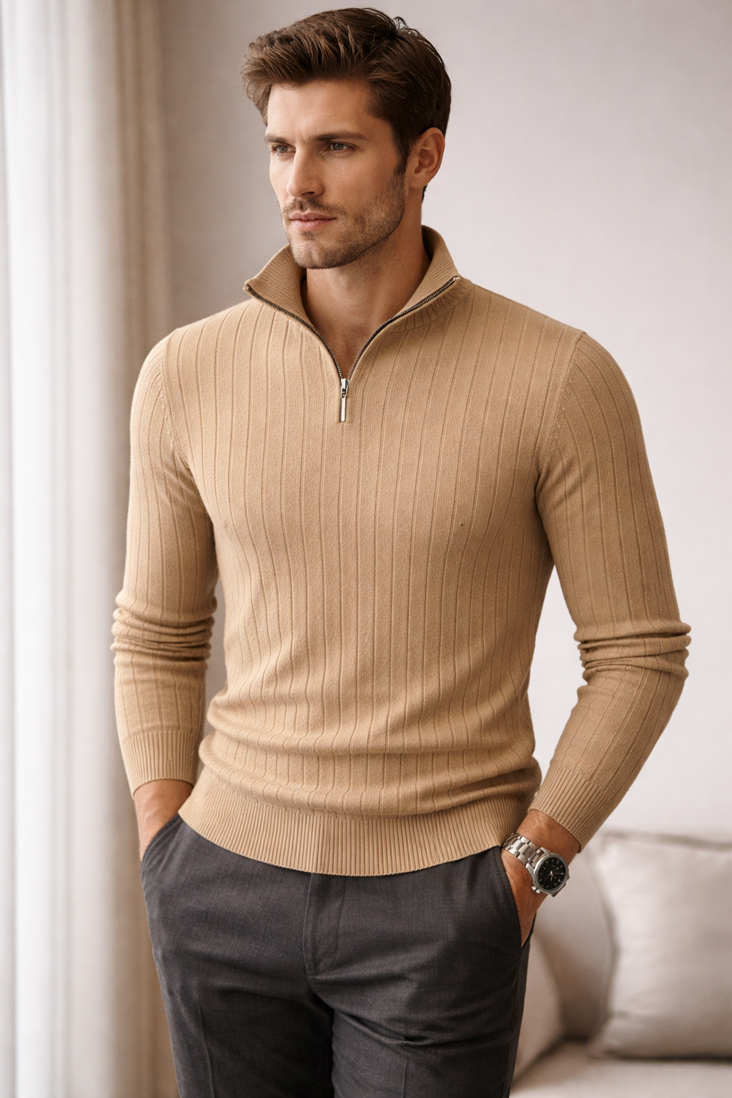 Man wearing a beige ribbed sweater with a zipper and dark pants indoors.